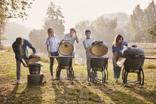 Patru kamado-uri Grill Guru Original de dimensiuni diferite, afara in natura, cu persoane langa ele.