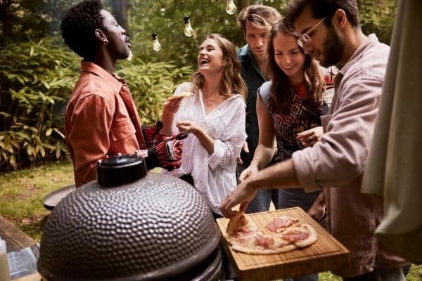 Tineri in gradina cu kamado Original Large de la Grill Guru si pizza p masuta laterala a gratarului.